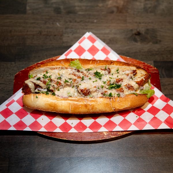A Made from Skratch Pizza Kitchen sub sandwich with chicken, sauce, cheese, and parsley on a red and white checkered paper.