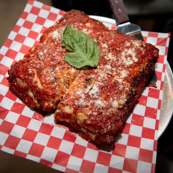 Deep dish pizza slice with red sauce, parmesan, and basil on checkered paper.