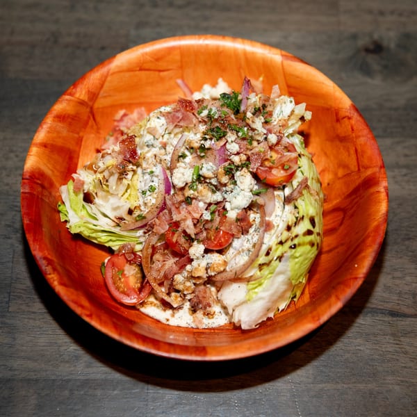 Wedge salad with blue cheese, bacon, tomatoes, and red onion in a rustic orange bowl.