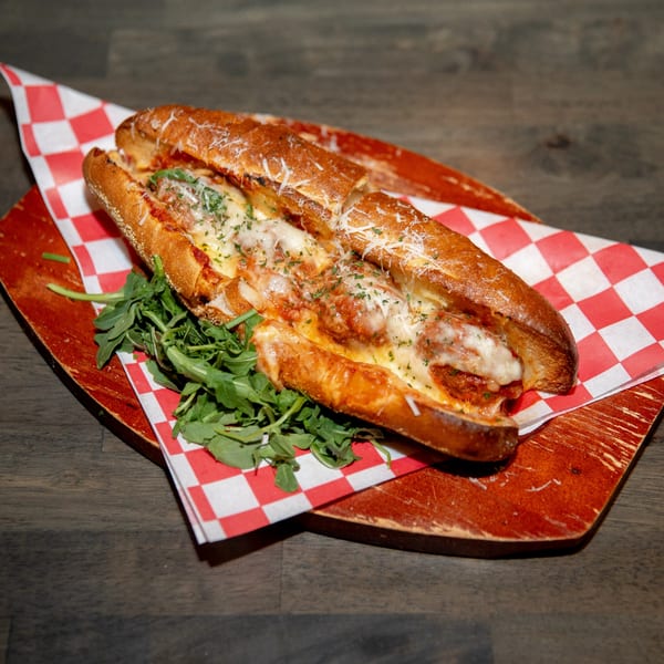 Meatball sub with melted cheese and parsley, served on a red and white checkered paper.