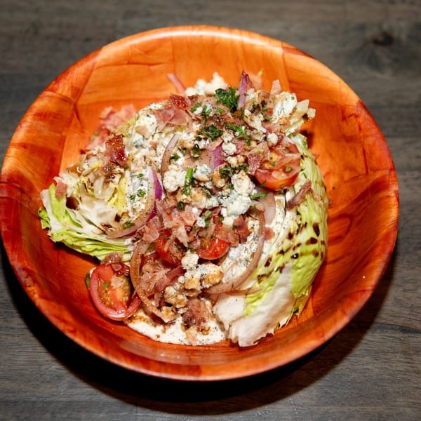 Wedge salad with bacon, blue cheese, red onion, tomatoes, and balsamic glaze in a wooden bowl.